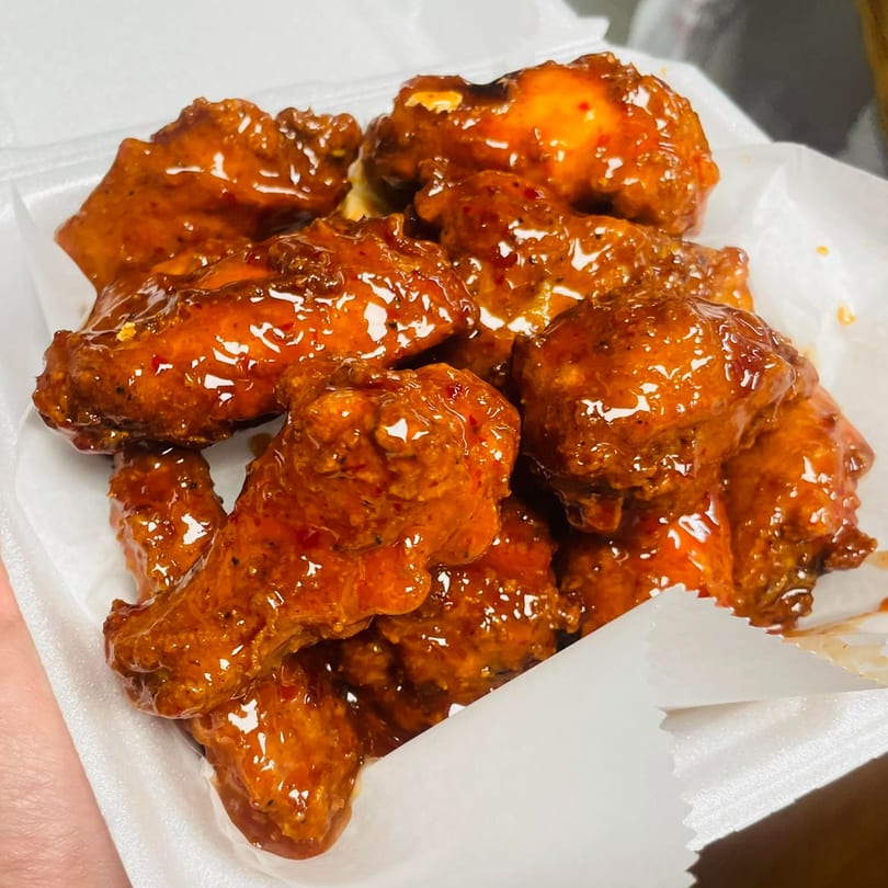 A close-up of Oishii Hibachi Grill's glistening, saucy chicken wings in a white takeout container.