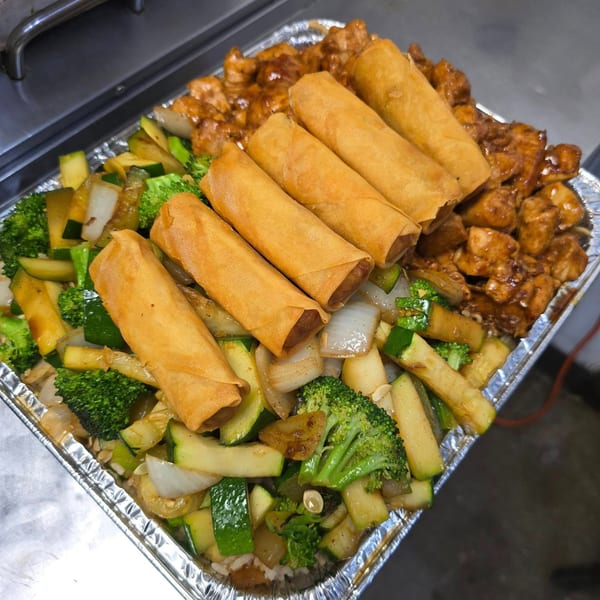 A catering tray of Oishii Hibachi Grill's chicken, egg rolls, and mixed vegetables with rice.