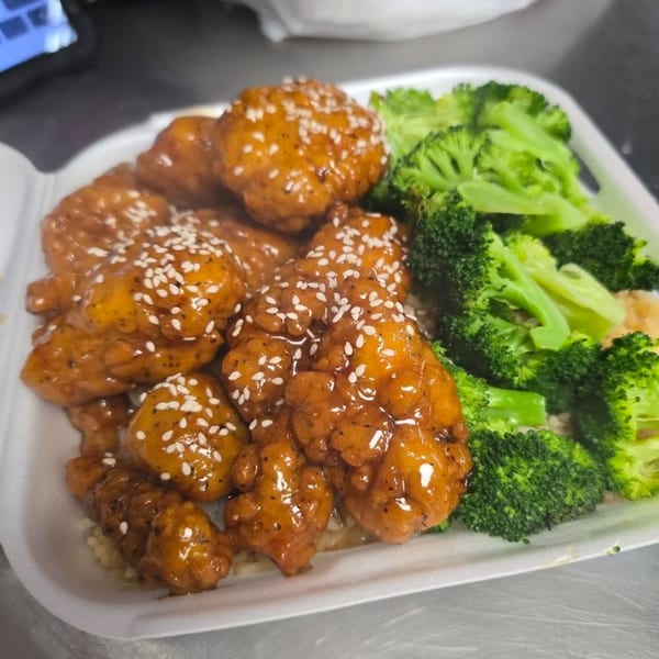 Oishii Hibachi Grill's sesame chicken with broccoli and rice, served in a white takeout container.